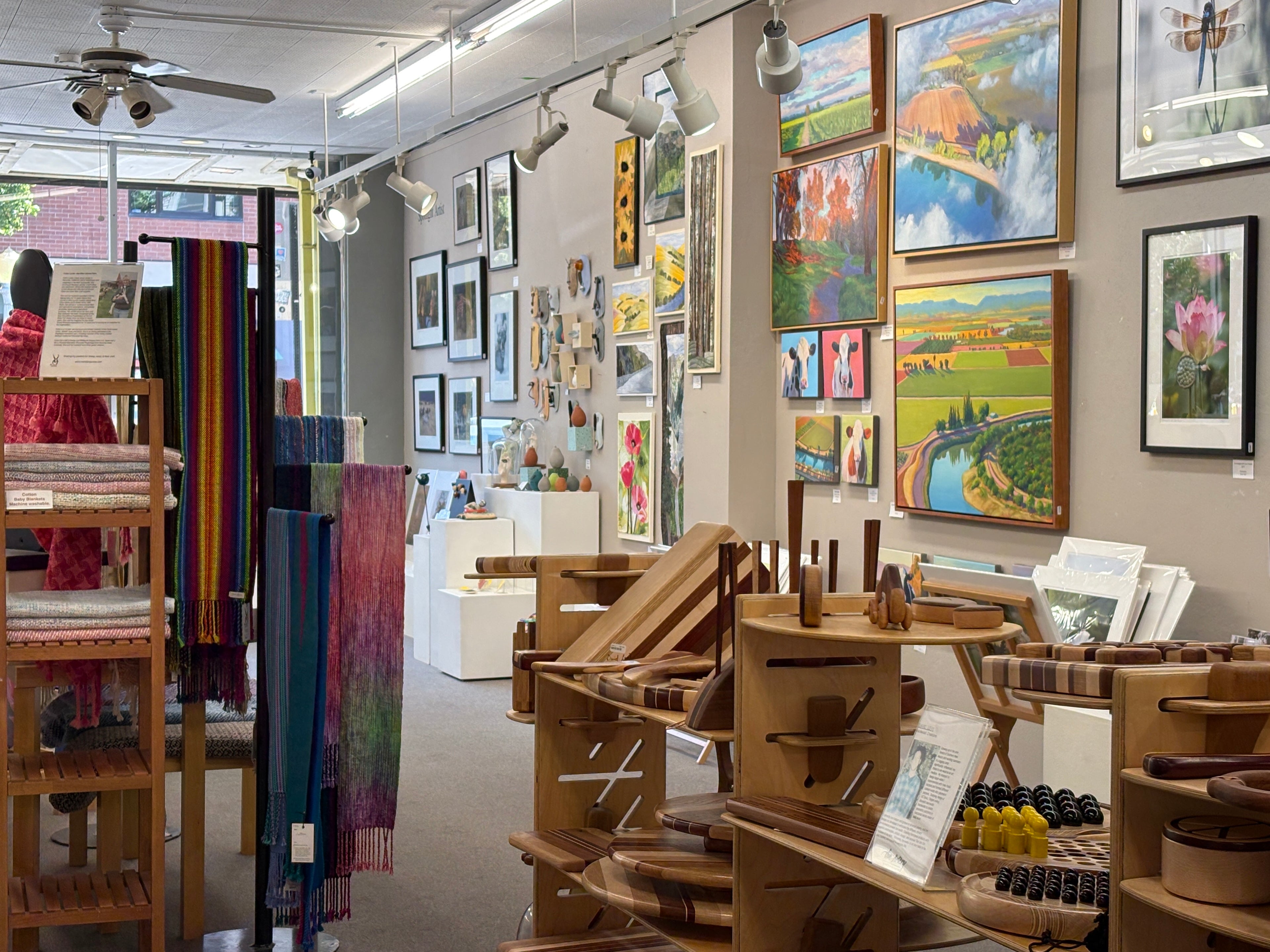 Art gallery with various artworks on the walls and wooden furniture on display.